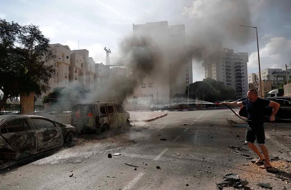 Un residente apaga vehículos en llamas en la ciudad israelí de Ashkelon tras el lanzamiento de cohetes desde Gaza, 7 de octubre de 2023 (EFE)