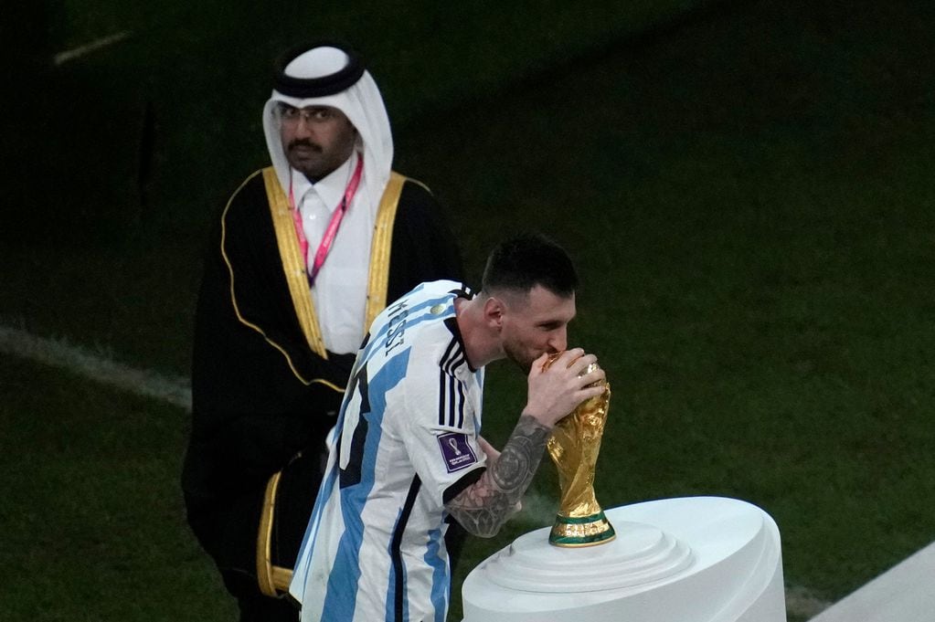 Lionel Messi besando la copa del mundo ante la mirada de unos de los organizadores qataríes. (AP)
