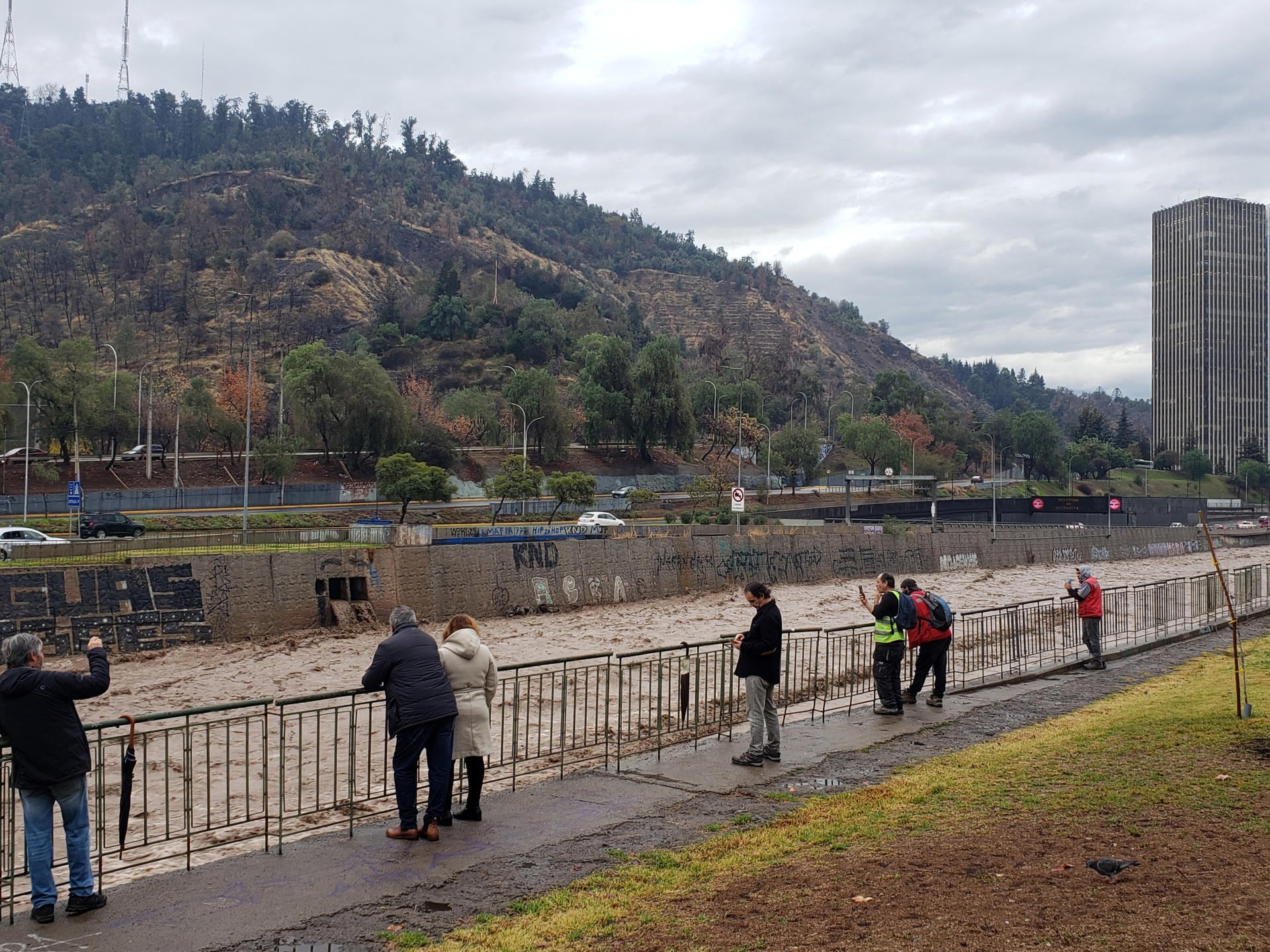 CH0. SANTIAGO (CHILE), 23/06/2023.- Personas observan hoy el elevado caudal del río Mapocho, producto de las intensas lluvias en Santiago (Chile). EFE/ Javier Martín
