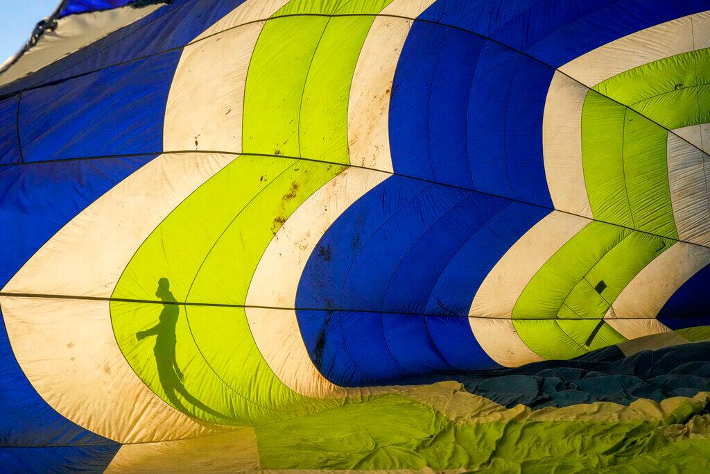 La sombra de un miembro de la tripulación se refleja en la lona de un globo aerostático durante la primera edición del Cumbres Ballon Festival 2022, en el parque El Trapiche de Peñaflor, a las afueras de Santiago, Chile, el 5 de febrero de 2022. (AP Foto/Esteban Félix)