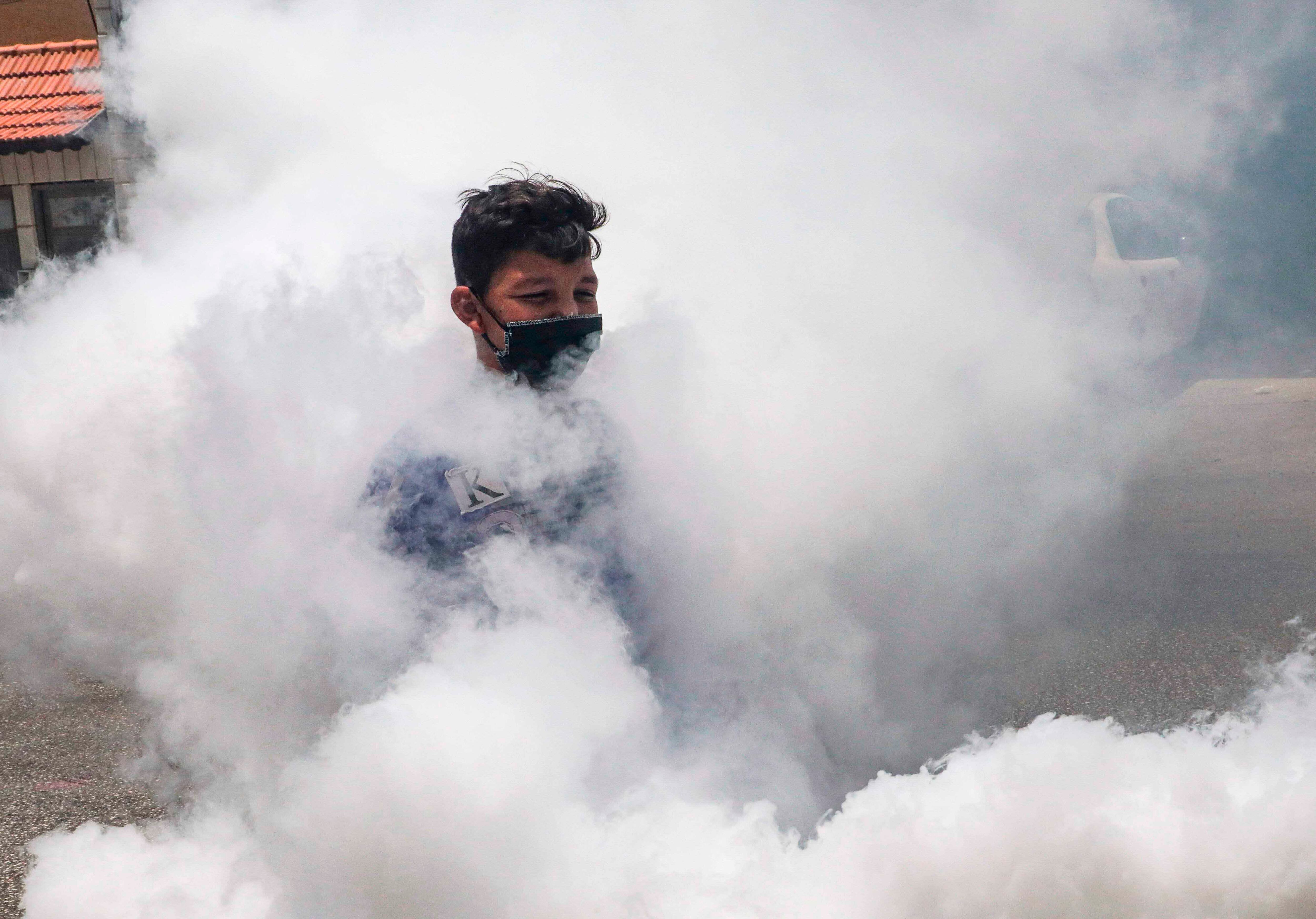 Un niño palestino vestido con una máscara es visto a través de los vapores de un vehículo del municipio de Hebrón que fumiga una calle en la ciudad de Hebrón en la Cisjordania ocupada el 24 de junio de 2020, después de un reciente aumento de casos de coronavirus COVID-19. / AFP / HAZEM BADER