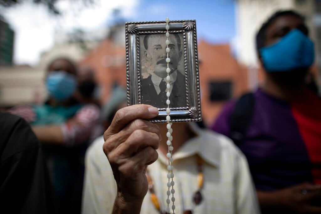 Una devota sostiene una imagen enmarcada del fallecido doctor José Gregorio Hernández en el exterior de la iglesia de La Candelaria donde están enterrados sus restos, en Caracas, Venezuela.