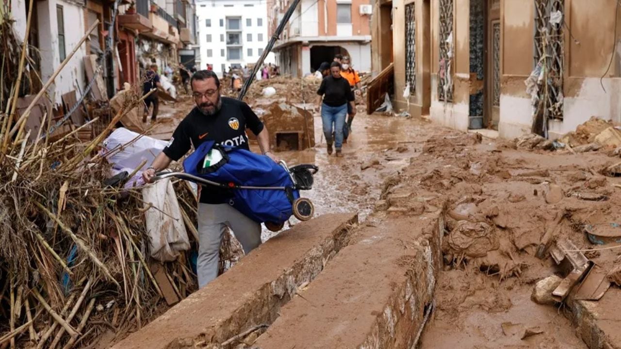 Un vecino lleva en volandas un carro de la compra entre el fango y escombros en la localidad de Paiporta. EFE/ Biel Aliño