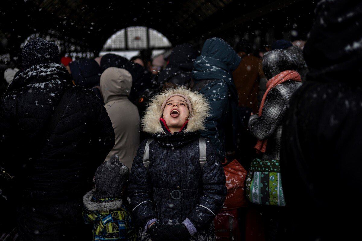 Una niña atrapa copos de nieve mientras espera junto a otros a subir a un tren hacia Polonia, en la estación de tren de Lviv, al oeste de Ucrania.