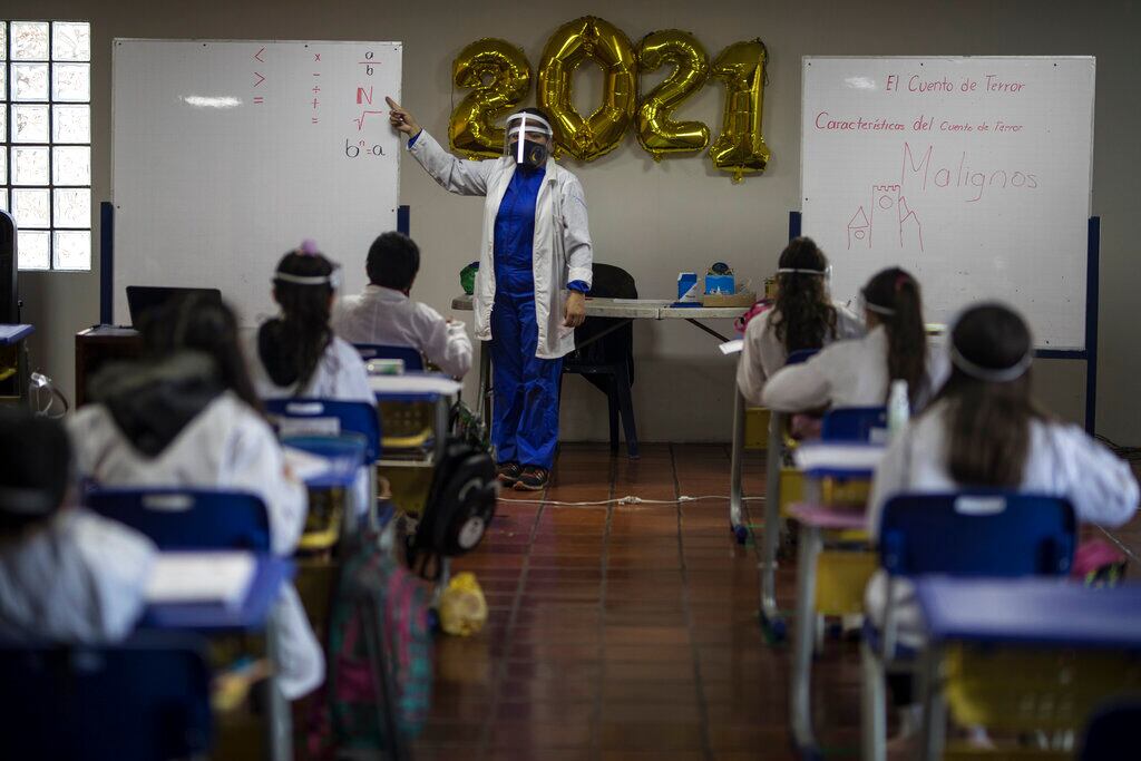 Una profesora de matemáticas da clase ante sus alumnos, todos vestidos con trajes de protección contra el coronavirus, en su primer día de clases presenciales desde marzo de 2020, en el Liceo Lunita, una escuela privada en Chia, a las afueras de Bogotá, Colombia