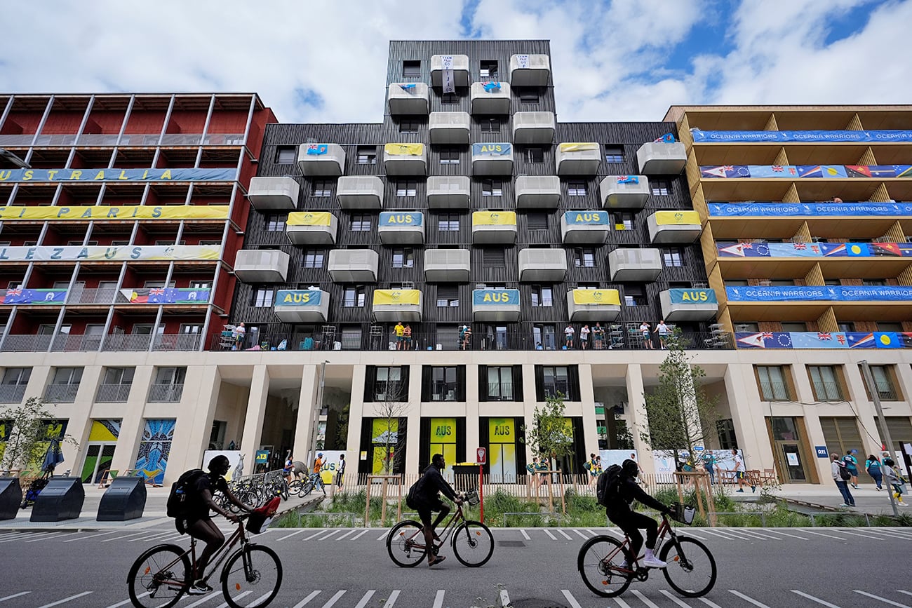 La gente anda en bicicleta frente a la residencia del equipo de Australia en la Villa Olímpica. (AP)