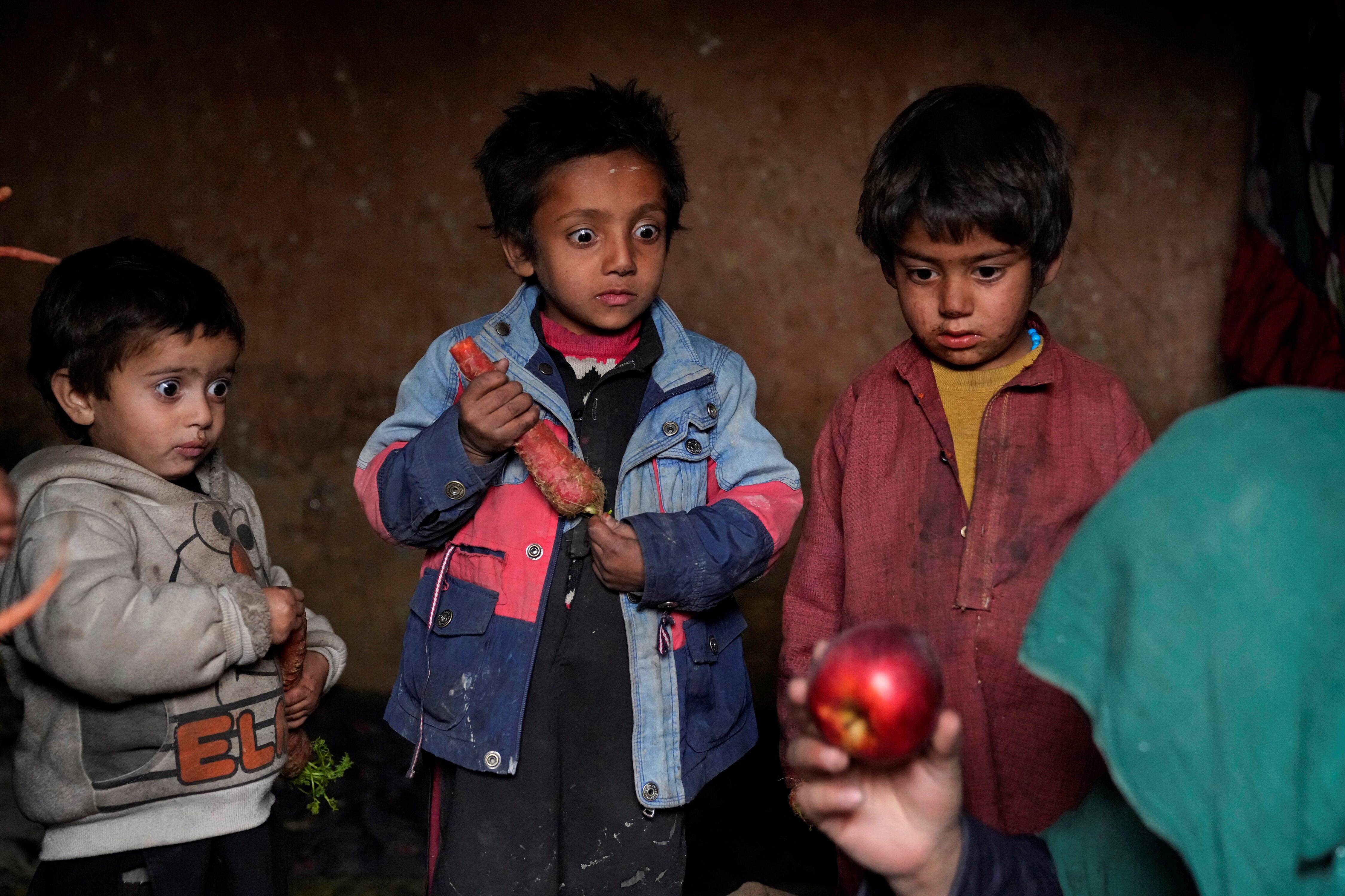 Esta imagen proporcionada por World Press Photo es parte de una serie titulada Afganistán al límite de Ebrahim Noroozi, Associated Press, que ganó la categoría Serie Asia de World Press Photo y muestra: Desde la caótica toma de Kabul por los talibanes el 15 de agosto de 2021, una economía ya devastada por la guerra que alguna vez se mantuvo viva sólo gracias a donaciones internacionales está ahora al borde del colapso. No hay suficiente dinero para los hospitales. La Organización Mundial de la Salud advierte que millones de niños sufren desnutrición y la ONU dice que el 97% de los afganos pronto vivirán por debajo del umbral de pobreza. Tres niños afganos desplazados internos miran con sorpresa una manzana que su madre trajo a casa después de mendigar, en un campamento en las afueras de Kabul, Afganistán, el jueves 2 de febrero de 2023. (Foto AP/Ebrahim Noroozi)