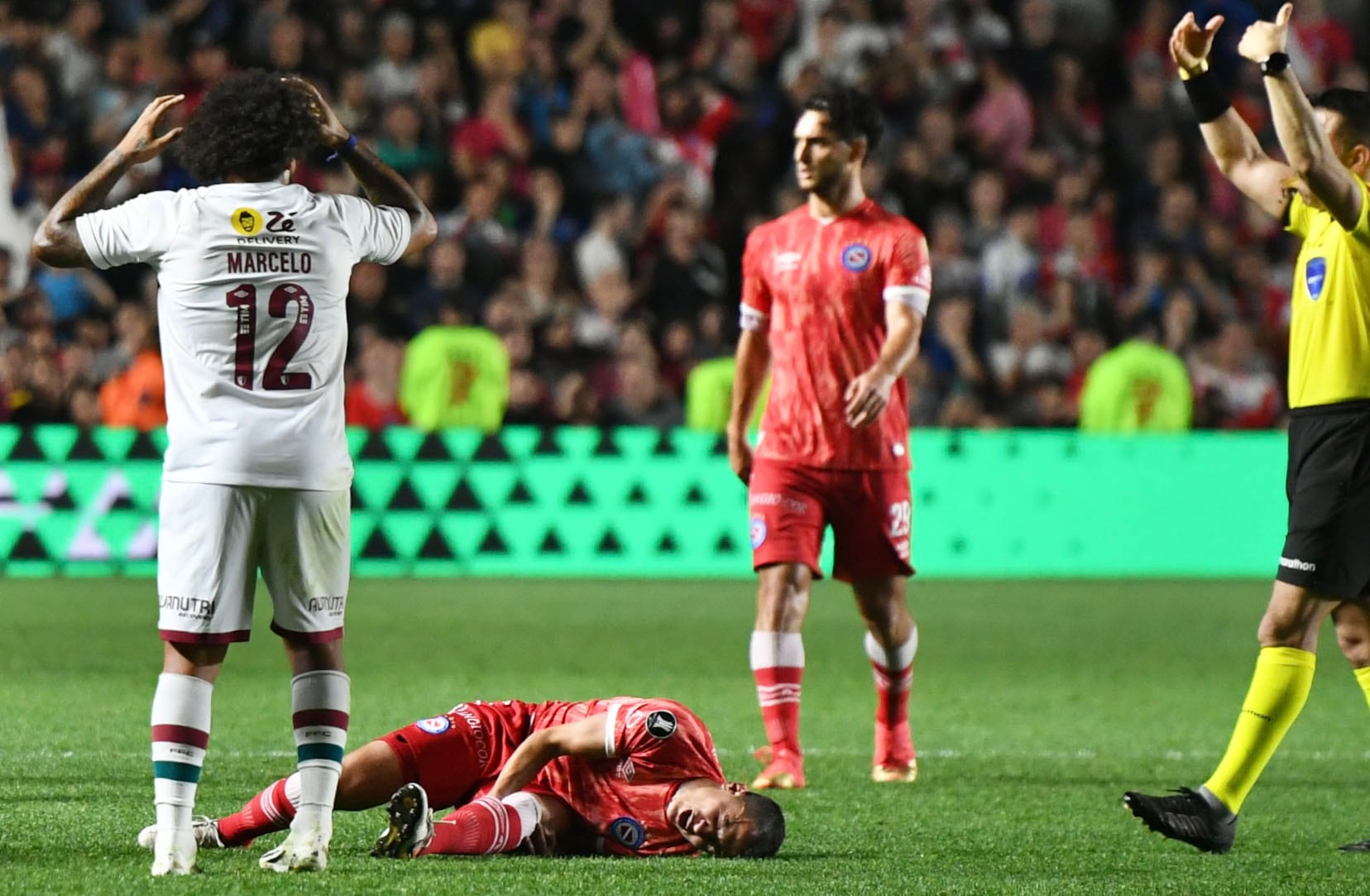 El defensor de Argentinos Juniors Luciano Sánchez y la dura lesión en la rodilla, y el lamento de Marcelo, el experimentado jugador de Fluminense. (Fotobaires)