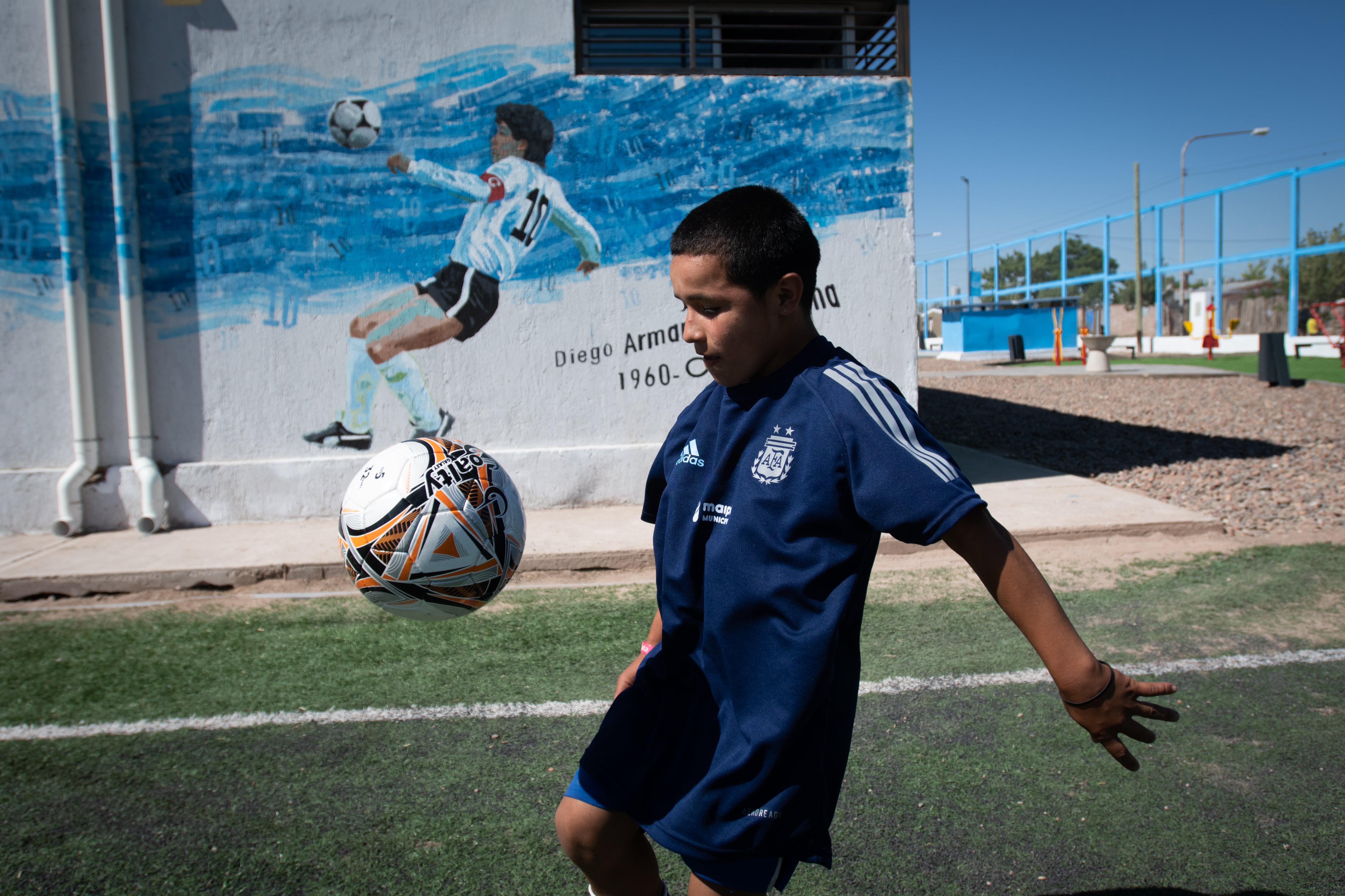 Matias Morales y la pelota el día de la inauguración de un mural de Diego Maradona de fondo. 



