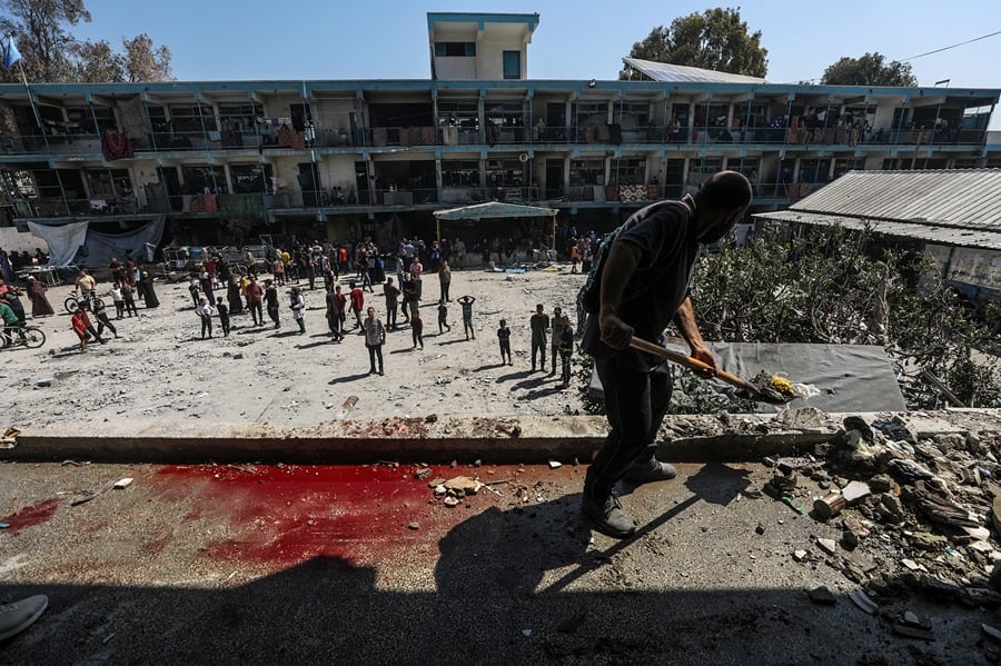 Un palestino limpia escombros mientras otros inspeccionan la escuela de la UNRWA destruida tras un ataque aéreo israelí en el campo de refugiados de Al Nusairat, en el centro de la Franja de Gaza (EFE)