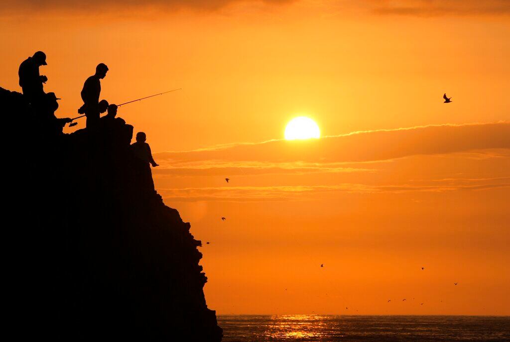 La silueta de varios pescadores se recorta contra el cielo al atardecer, en la playa de Herradura, en Lima, Perú