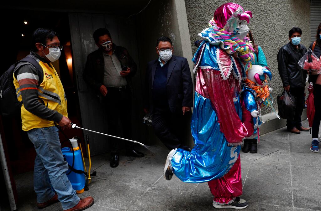 Un operario municipal rocía con desinfectante a una persona disfrazada de Pepino en plena pandemia del coronavirus, antes de su entrada al concurso para elegir a los tres personajes más queridos del Carnaval _ Chuta, Pepino y Chola, que representan la alegría _ en La Paz, Bolivia