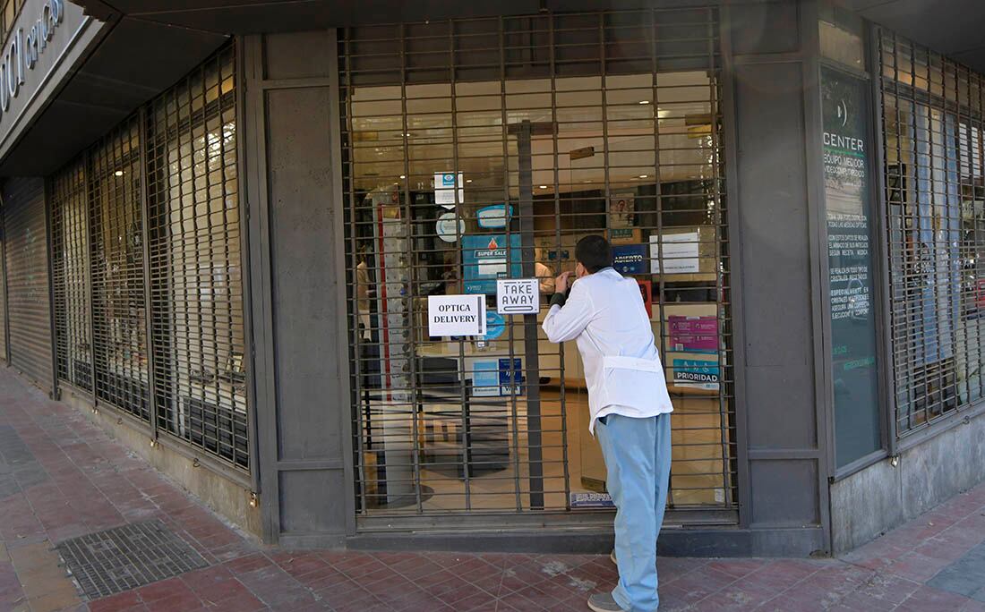 Una óptica atiende a sus clientes con las persianas bajas debido a las restricciones impuestas por el gobierno.