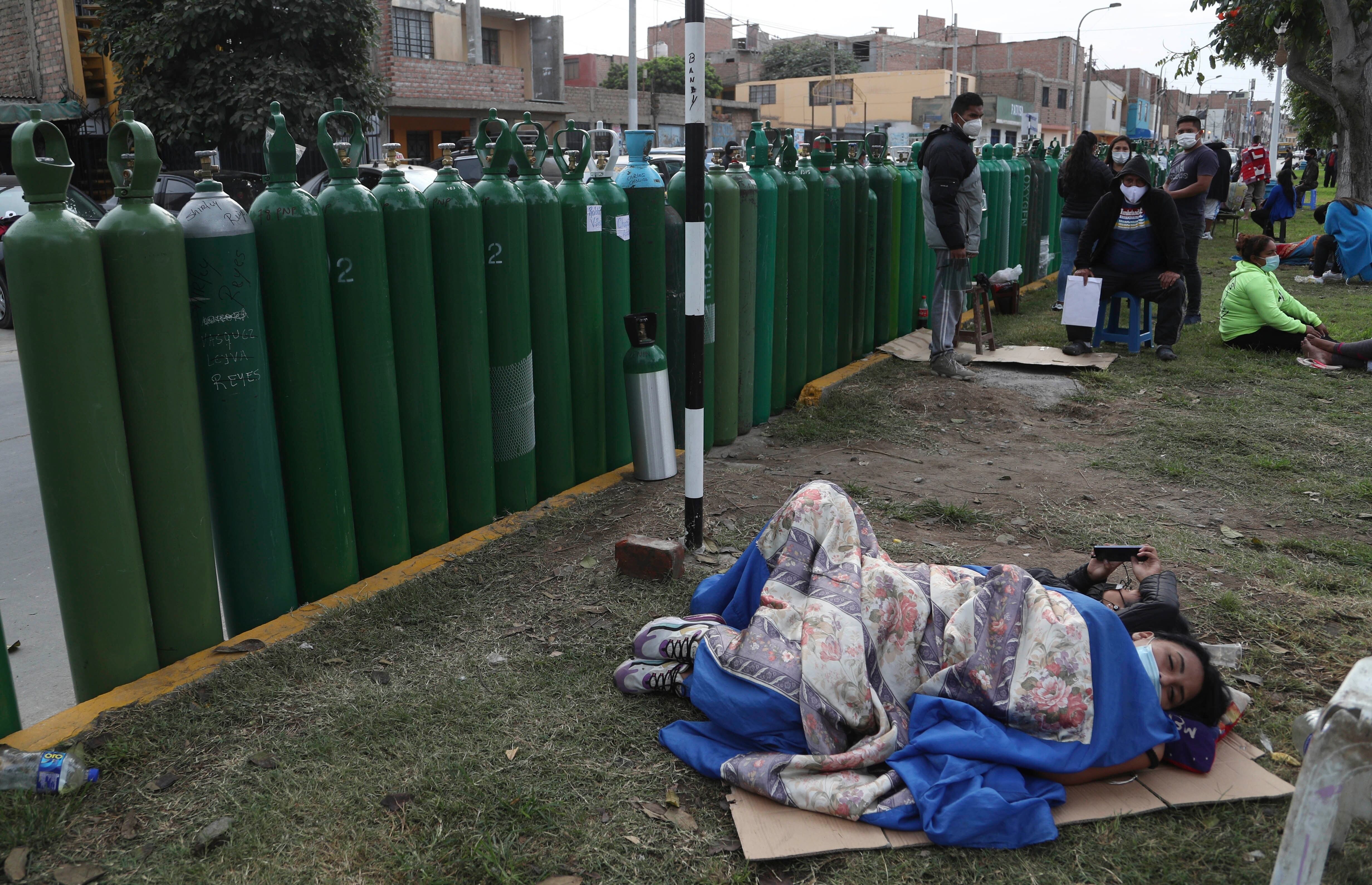 Varias personas esperan tendidas en el suelo junto a sus botellas de oxígeno vacías a que abra un establecimiento para rellenarlas, en Callao, Perú