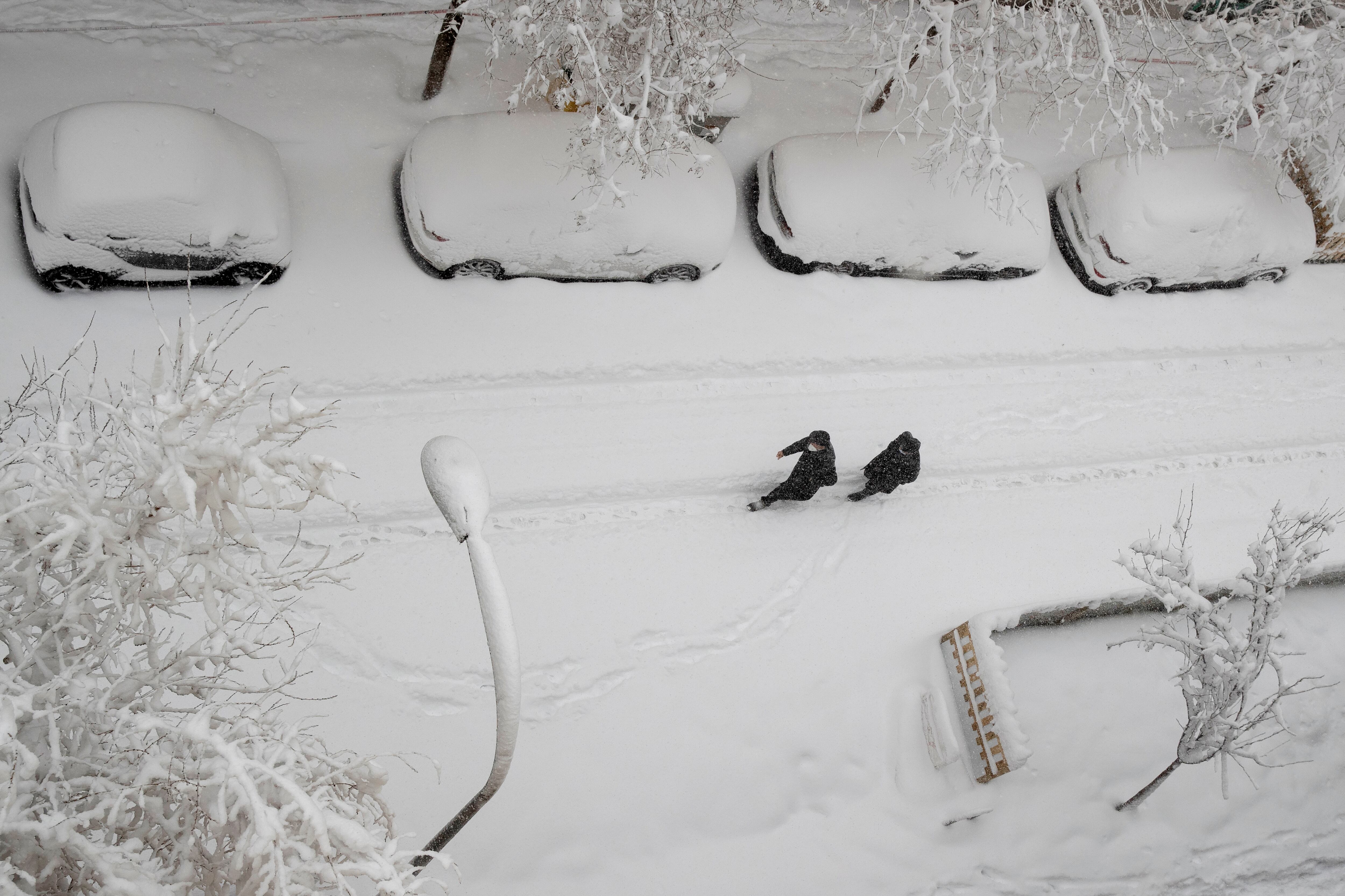 Dos hombres caminan por una calle cubierta de nieve tras una fuerte nevada, en Madrid.