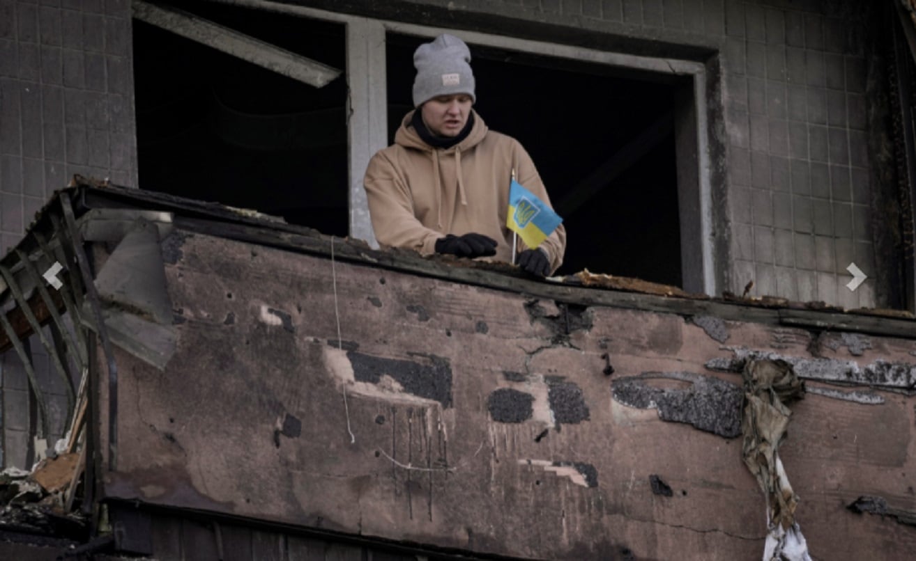 Un hombre coloca una pequeña bandera ucraniana en el balcón quemado de un apartamento en un bloque que fue destruido por un ataque de artillería en Kiev, Ucrania, el lunes 14 de marzo de 2022. (AP)