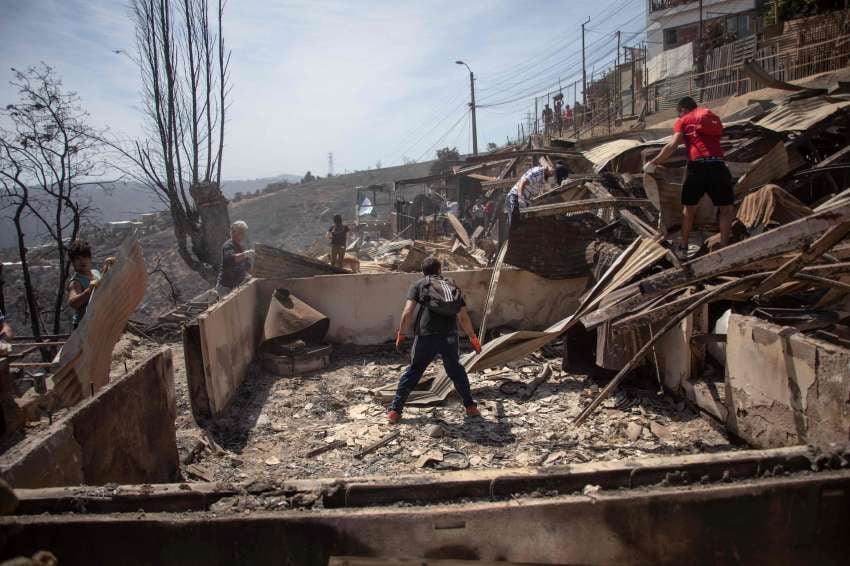 
Los lugareños buscan pertenencias personales después de un incendio forestal en el cerro Rocuant en Valparaíso | AFP
   