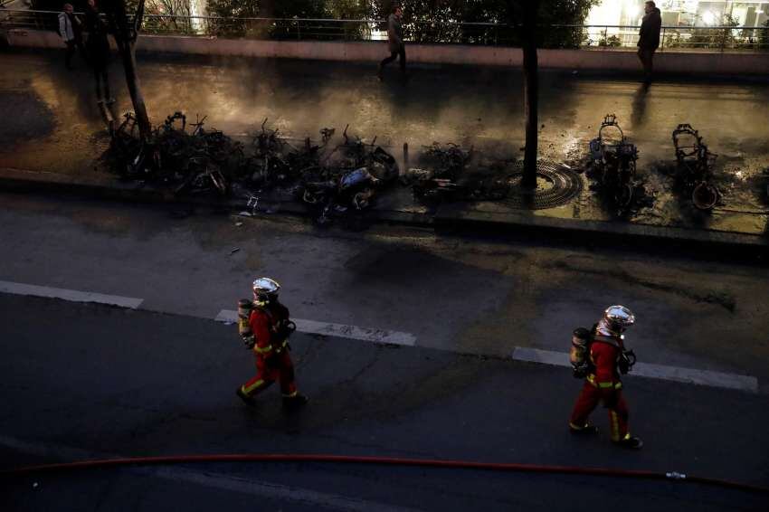 
Los bomberos pasan junto a vehículos carbonizados después del incendio | AP
   