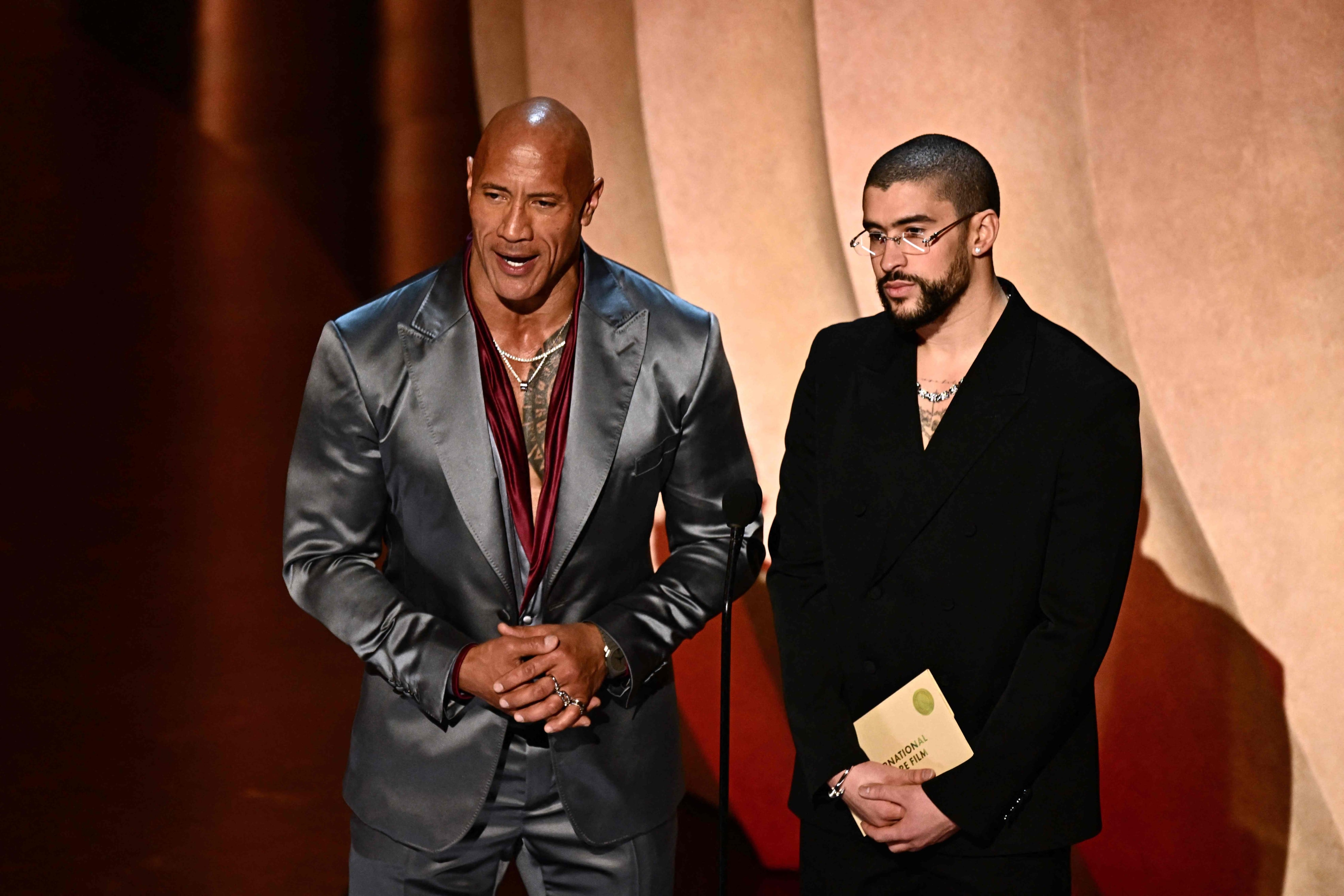 El actor estadounidense Dwayne Johnson (izq.) y el cantante puertorriqueño Bad Bunny presentan el premio a la Mejor Película Internacional en el escenario durante la 96a edición anual de los Premios de la Academia en el Dolby Theatre de Hollywood, California, el 10 de marzo de 2024. (Foto de Patrick T. Fallon / AFP)