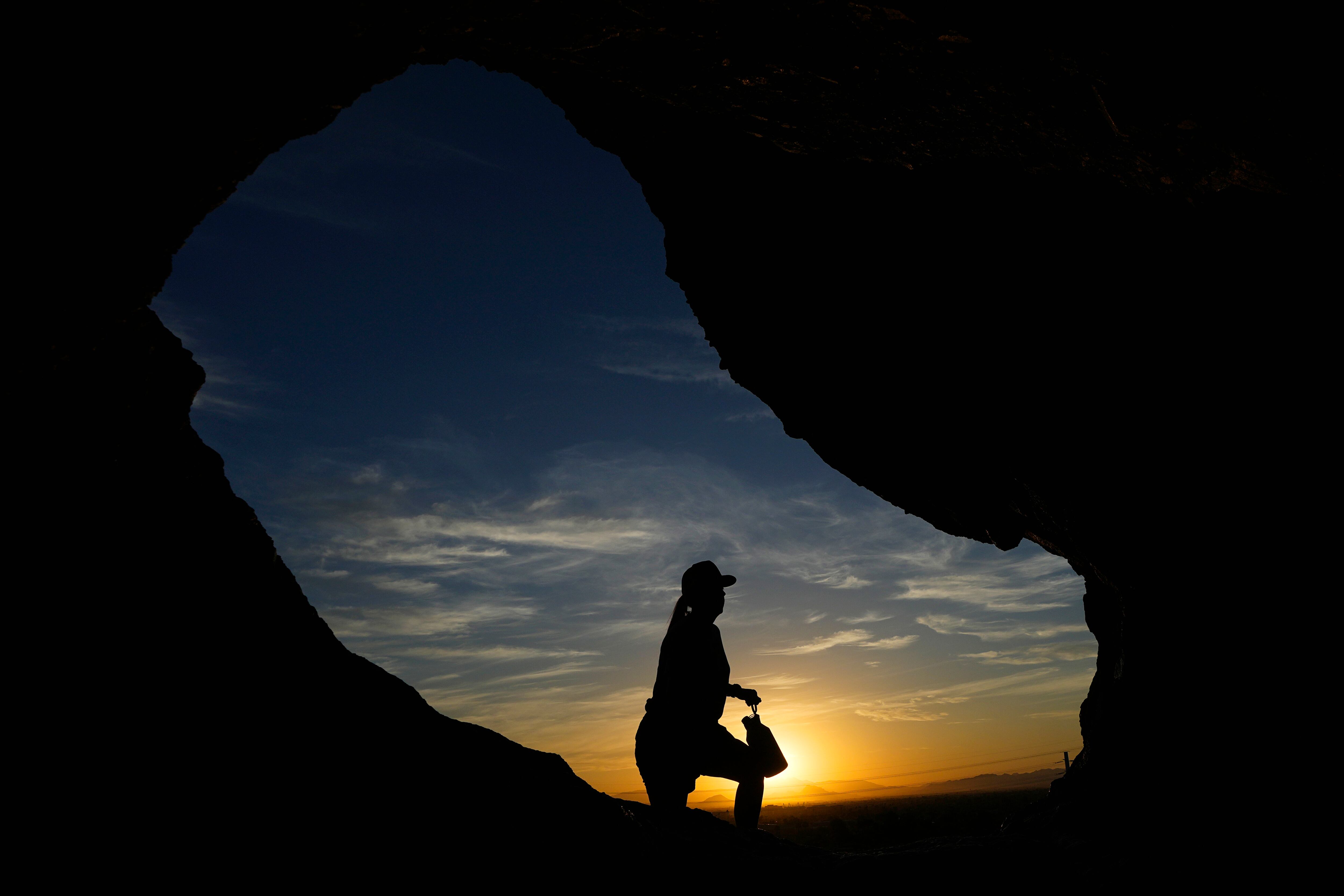 ARCHIVO - Un senderista pasa frente a la caverna Hole-in-the-Rock de Papago Park al amanecer, Phoenix, 17 de julio de 2023. Los científicos dicen que las causas principales del reciente calor extremo son el cambio climático provocado por el ser humano y el fenómeno natural El Niño. Pero algunos dicen que necesariamente hay algo más. (AP Foto/Ross D. Franklin, File)