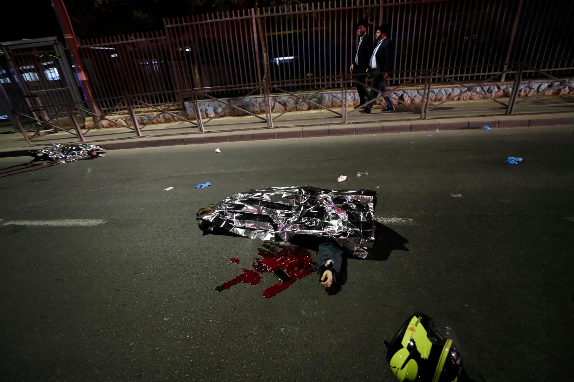 Dos hombres caminan más allá de los cuerpos cubiertos de las víctimas mientras los servicios de emergencia trabajan en la escena de un tiroteo en una sinagoga en el área de Neve Yaakov en Jerusalén. Foto: EFE/EPA/ATEF SAFADI