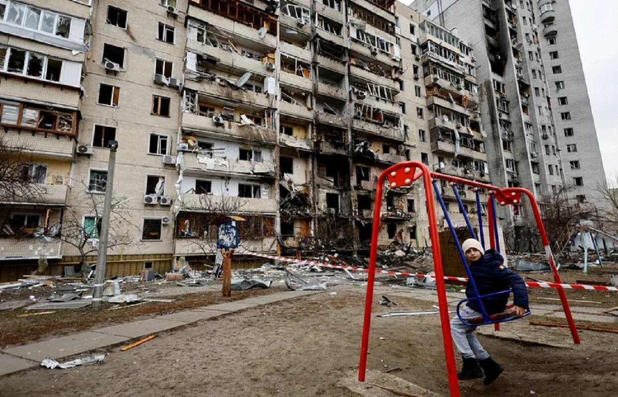 Un nene se sienta en un columpio frente a un edificio residencial dañado en Kiev, Ucrania, este viernes 25 de febrero de 2022. (Gentileza)