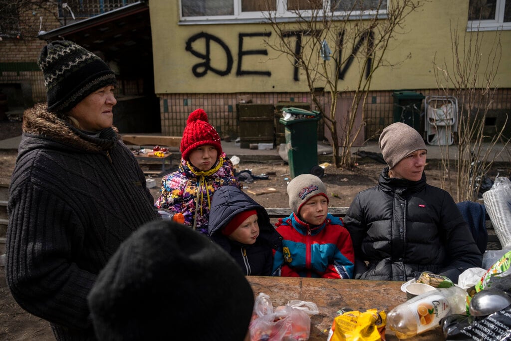 En esta imagen de archivo, vecinos esperan el reparto de comida en Bucha, a las afueras de Kiev, Ucrania, el 8 de abril de 2022. La pintada en la pared de la vivienda dice "NIÑOS". (AP Foto/Rodrigo Abd, archivo)