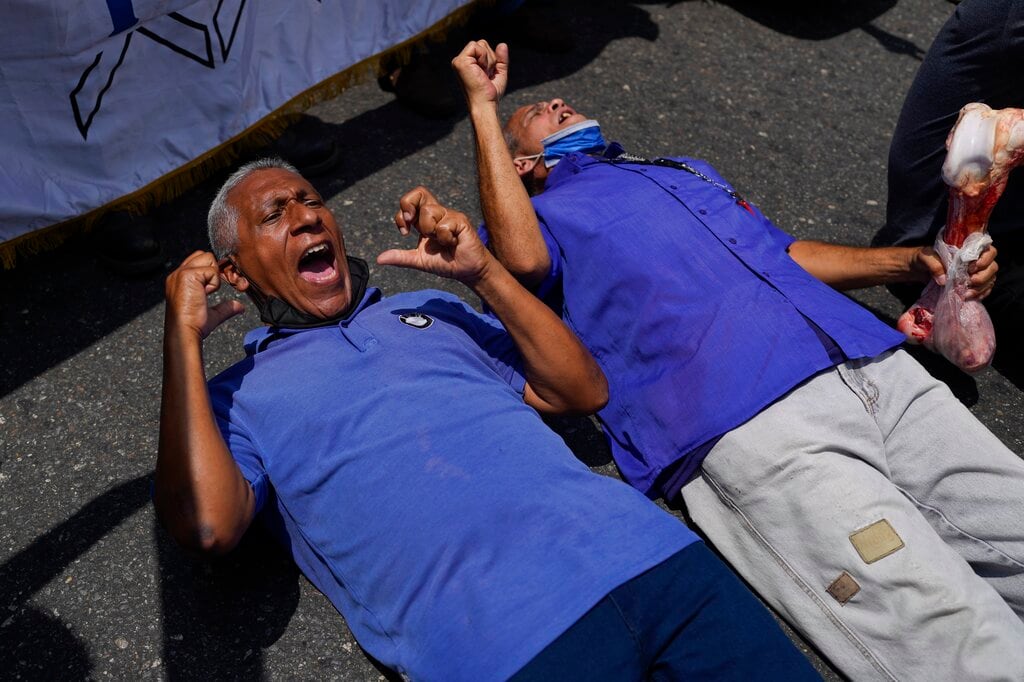 Dos personas tumbadas en el piso gritan lemas pidiendo mejoras salariales para los trabajadores y en las pensiones de los jubilados, durante una protesta en Caracas, Venezuela, el 6 de abril de 2022. (AP Foto/Ariana Cubillos)