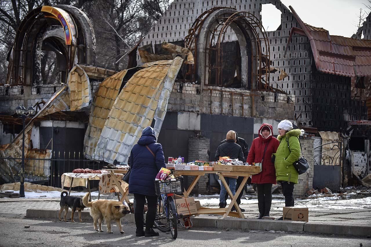 Personas venden productos en el mercado callejero junto a un edificio destruido. Foto: EFE