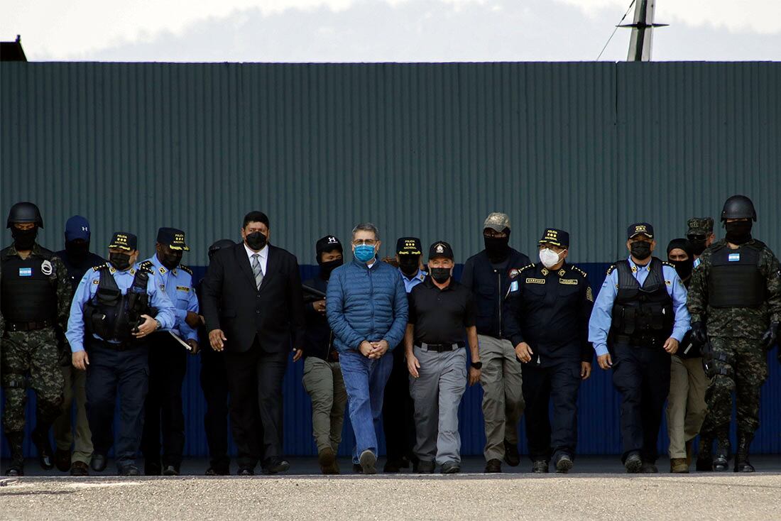 El expresidente de Honduras Juan Orlando Hernández (centro), con una mascarilla azul y grilletes en las manos, es escoltado por un fuerte dispositivo de seguridad a un avión en una base de la Fuerza Aérea en Tegucigalpa, Honduras, el 21 de abril de 2022. Honduras extraditó a Hernández a Estados Unidos para enfrentar cargos de tráfico de drogas y armas en un dramático revés para un político que en su día fue elogiado por las autoridades estadounidenses como un aliado clave en la lucha contra el narcotráfico. (AP Foto/Elmer Martínez)