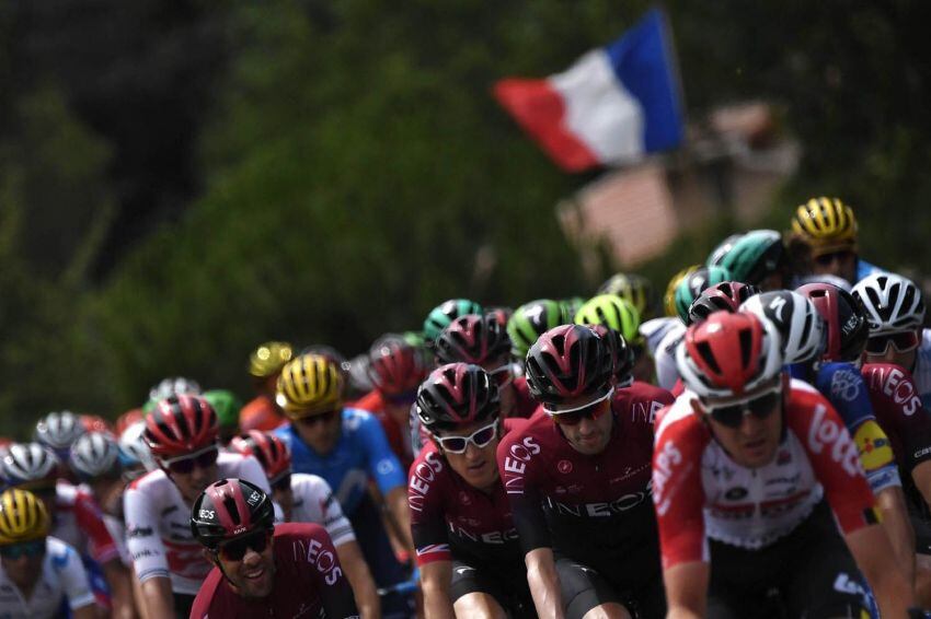 
Foto: AFP | El británico Geraint Thomas (C) lidera el pelotón mientras una bandera francesa flamea en segundo plano.
   