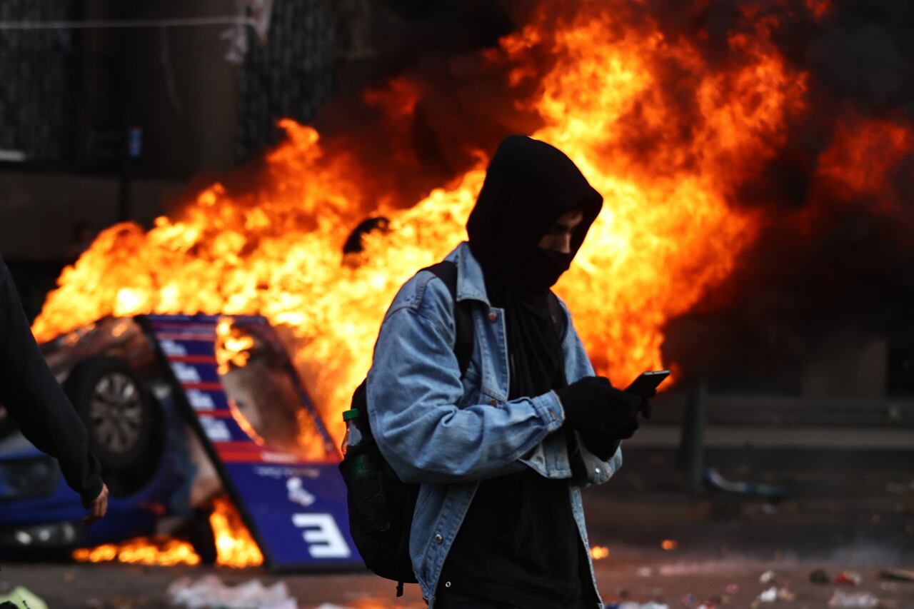 Una persona observa su celular mientras se da un incendio a sus espaldas durante enfrentamientos entre la policía y personas que protestan a las afueras del senado. Foto: EFE/ Juan Ignacio Roncoroni