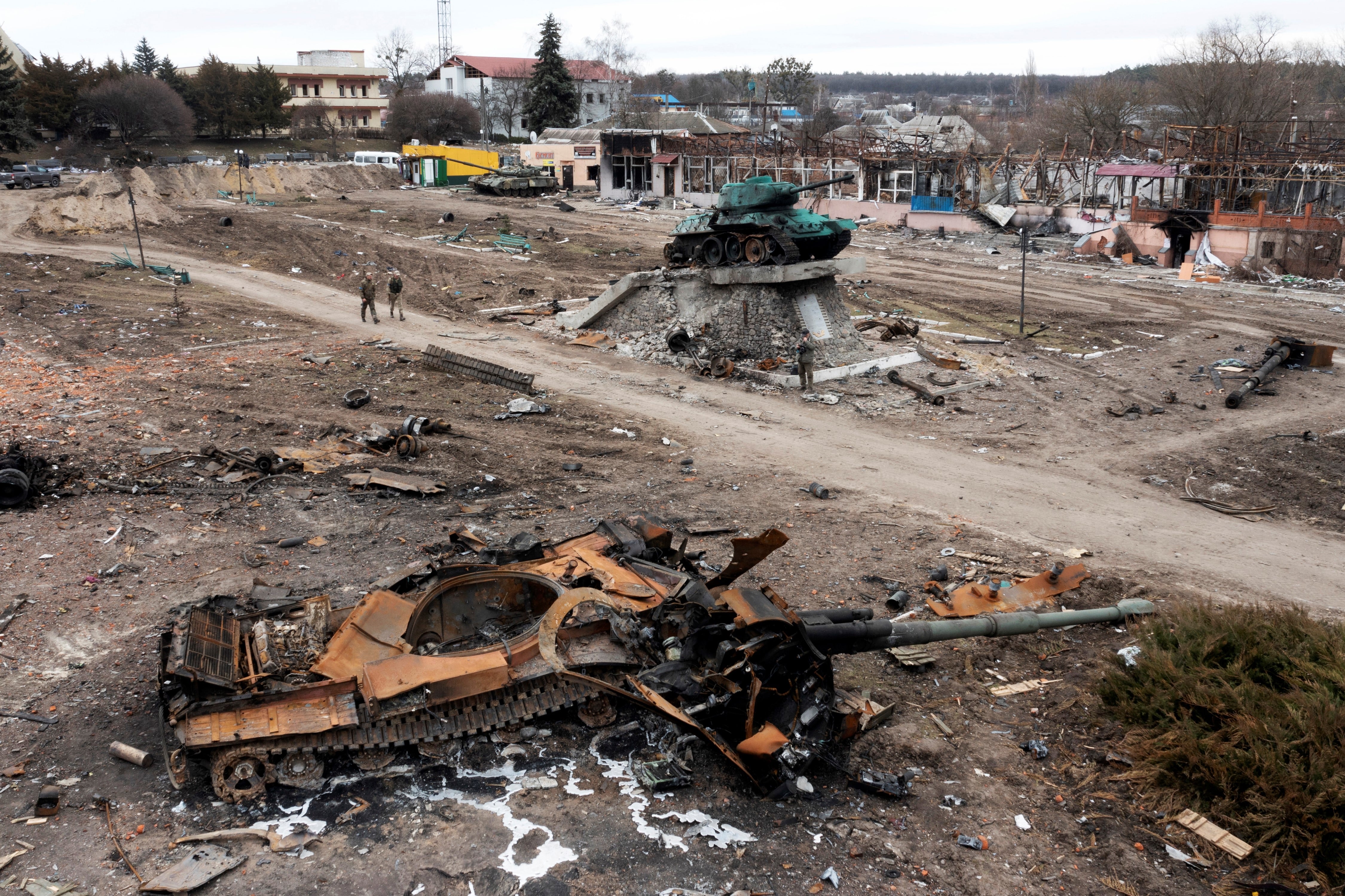 Los residentes locales pasan junto a un tanque ruso dañado en la ciudad de Trostyanets, al este de la capital, Kiev, Ucrania. El monumento a la Segunda Guerra Mundial se ve al fondo.