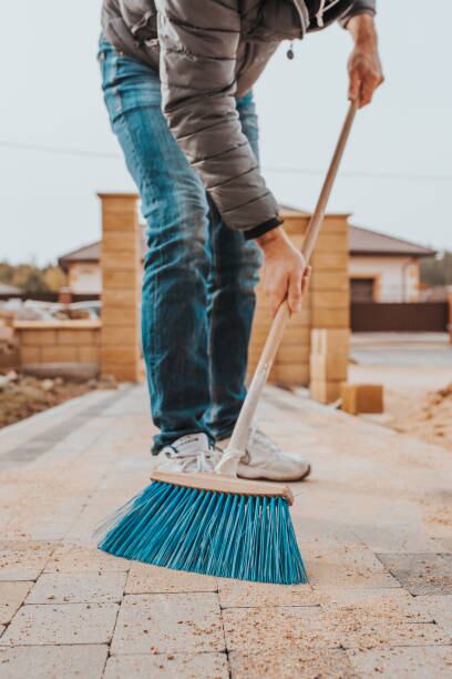 A man with a broom sweeps sand into the seams of paving slabs after laying