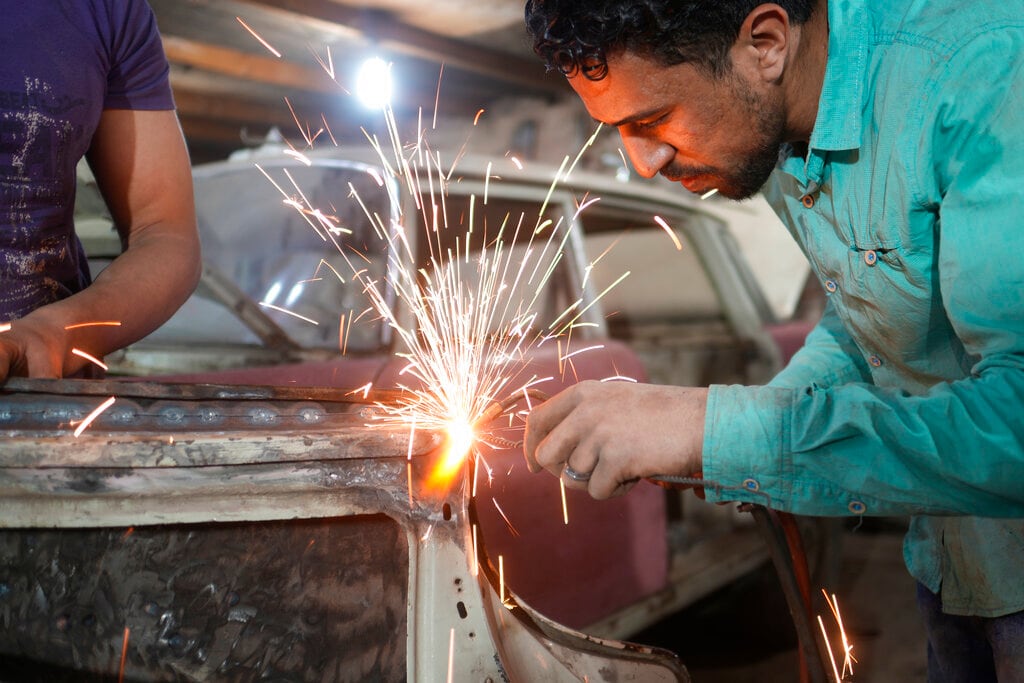 Abd Allah Ragab trabaja en la restauración de un Mercedes 1966 en el lote de un coleccionista privado el viernes 8 de abril de 2022, en la ciudad de El Saff, en las afueras de El Cairo, Egipto. Mohamed Wahdan, un empresario egipcio y coleccionista de vehículos clásicos, dice haber acumulado más de 250 automóviles vintage, antiguos y clásicos en los últimos 20 años. (AP Foto/Amr Nabil)