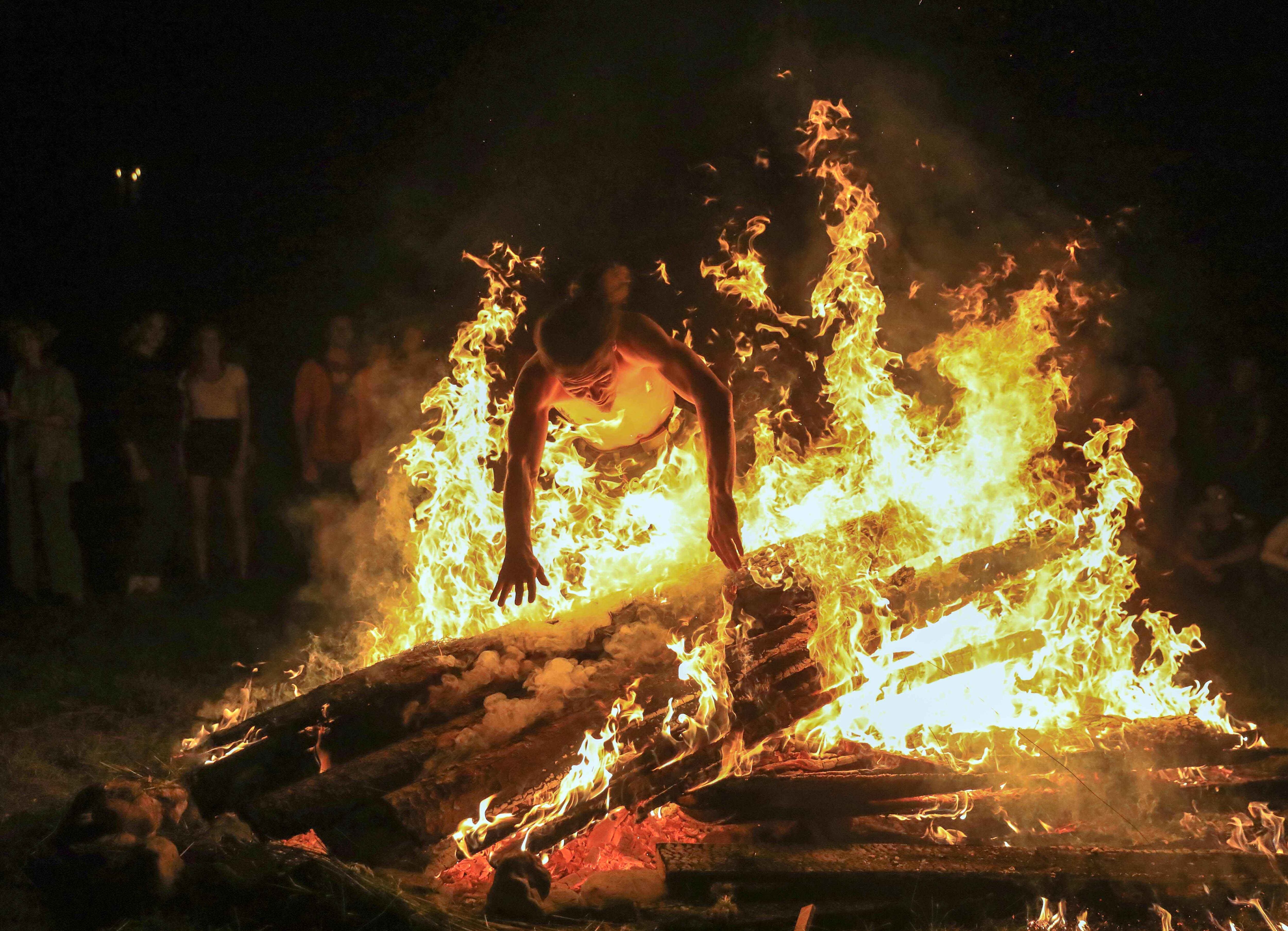 Un joven salta sobre el fuego mientras las personas participan en una celebración tradicional de la noche del solsticio de mediados de verano (Festival Rasos) en el Museo al aire libre de Lituania en Rumsiskes, al este de Kaunas, Lituania, a fines del 23 de junio de 2020. / AFP / PETRAS MALUKAS