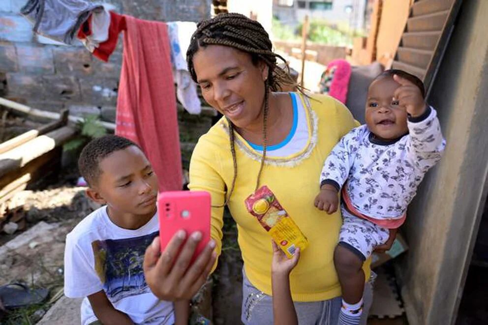 Miguel Barros escucha a su madre Celia mientras esta sostiene a su hermano menor Gael en su casa en Santa Luzia. Foto: AFP