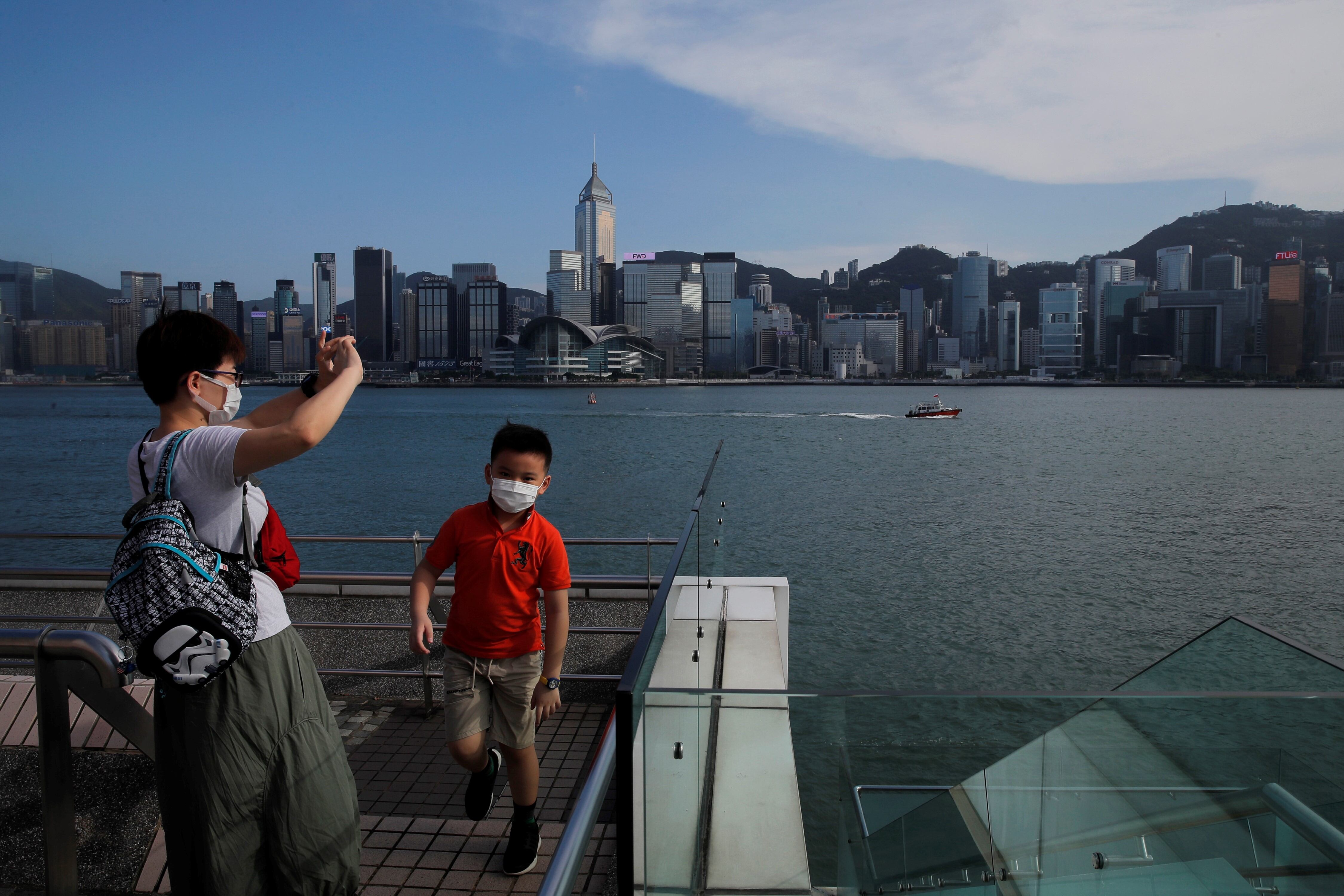 Personas con máscaras para protegerse contra el coronavirus, toman fotografías a lo largo de la costa del puerto de Victoria en Hong Kong. AP