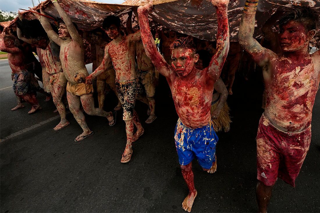 Indígenas, cubiertos de pintura roja _ que simboliza la sangre derramada de su comunidad _ y tierra _ representando el oro _, marchan durante una protesta contra el incremento de la minería en sus tierras, ante el Ministerio de Minas y Energía, en Brasilia, Brasil, el 11 de abril de 2022. (AP Foto/Eraldo Peres)