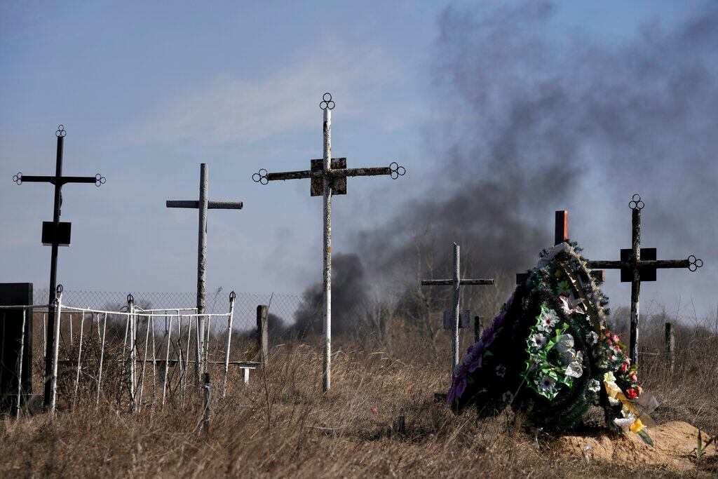 El humo de los proyectiles se eleva al fondo, una corona de flores honra a los caídos de la guerra en el cementerio de Vasylkiv, el suroeste de Kiev. Foto: AP / Vadim Ghirda