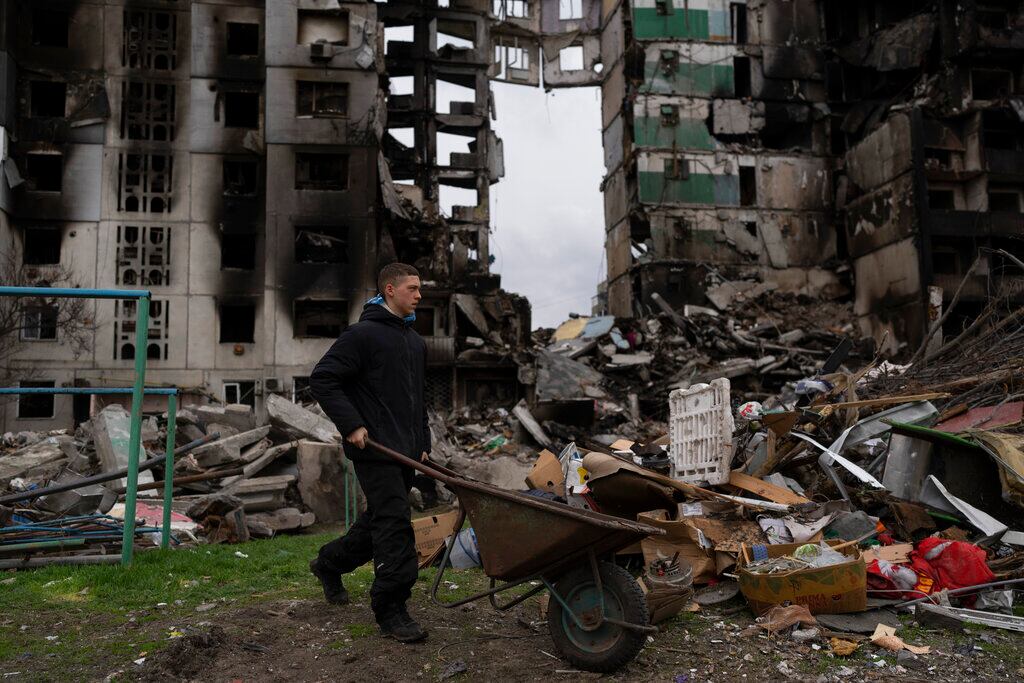 Un joven empuja una carretilla frente a un edificio residencial destruido, el domingo 10 de abril de 2022. 