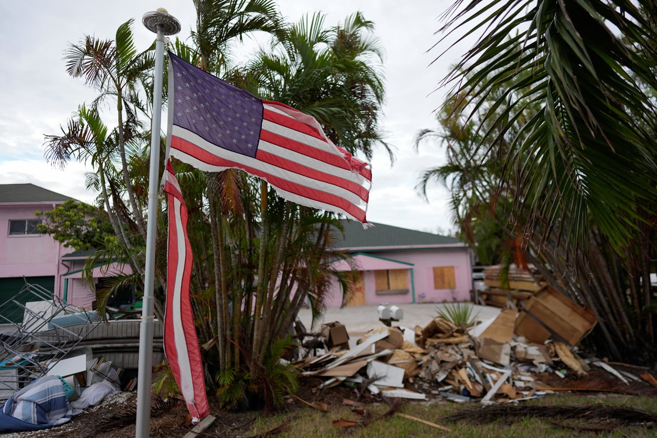 Una bandera estadounidense hecha harapo ondea afuera de una casa mientras muebles y artículos del hogar dañados por las inundaciones del huracán Helene (septiembre de 2024) / Gentileza