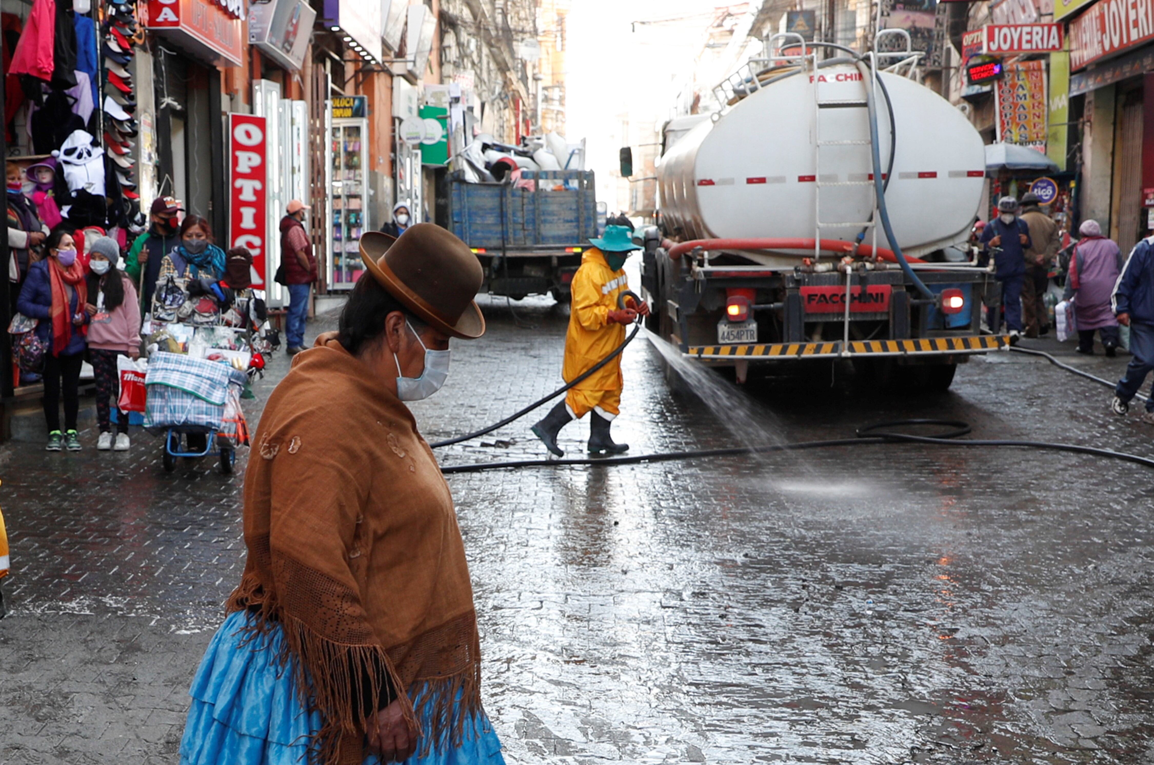 Una mujer pasa junto a trabajadores de la ciudad que desinfectan la calle en medio de la nueva pandemia de coronavirus en La Paz, Bolivia. AP