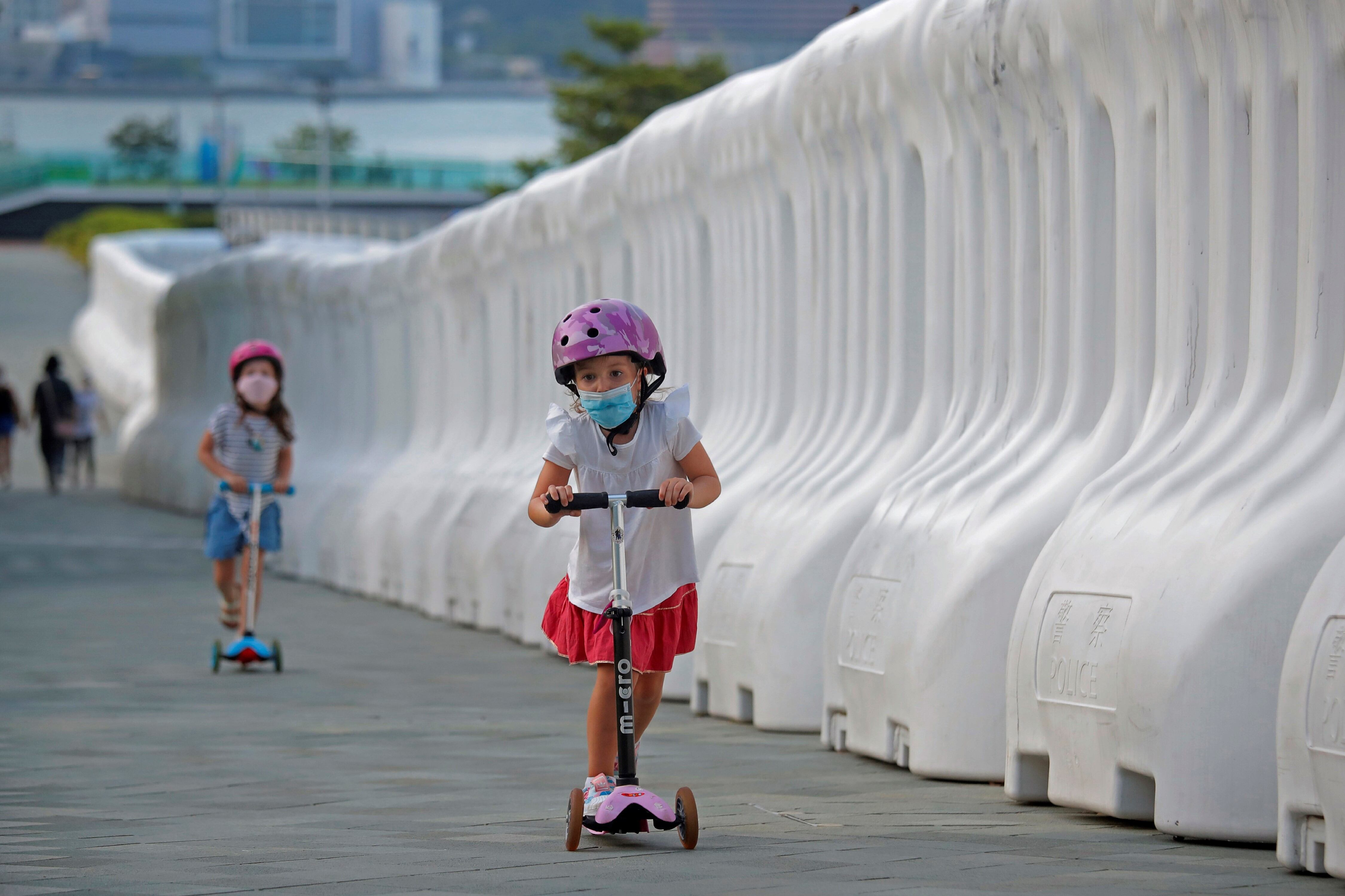 Niños con máscaras para protegerse contra el coronavirus, juegan junto a las barreras llenas de agua afuera de la Oficina del Gobierno de Hong Kong