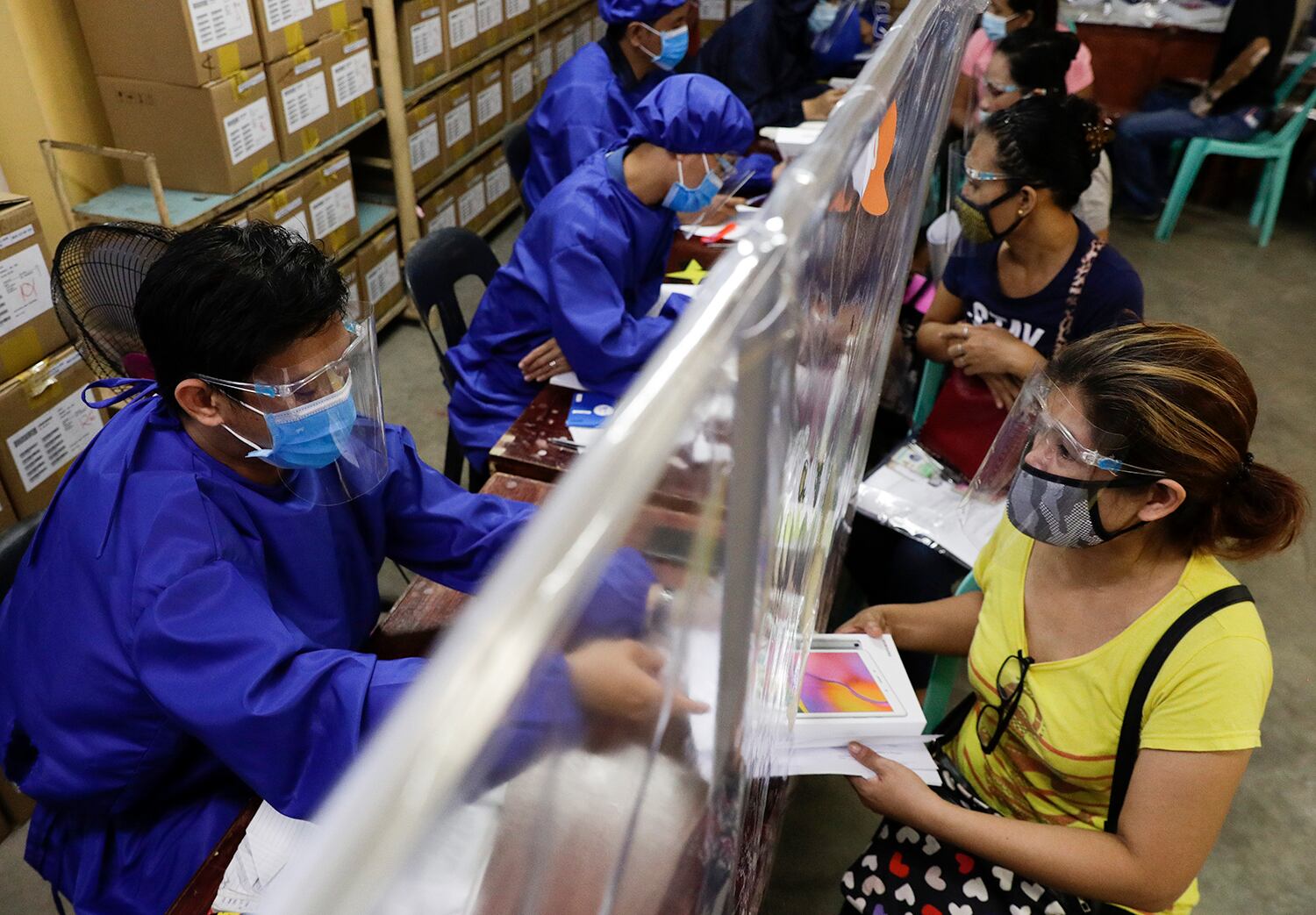 Una maestra con un traje protector entrega una tablet electrónica a una mujer mientras se preparan para las clases en línea en la ciudad de Quezón, Filipinas.