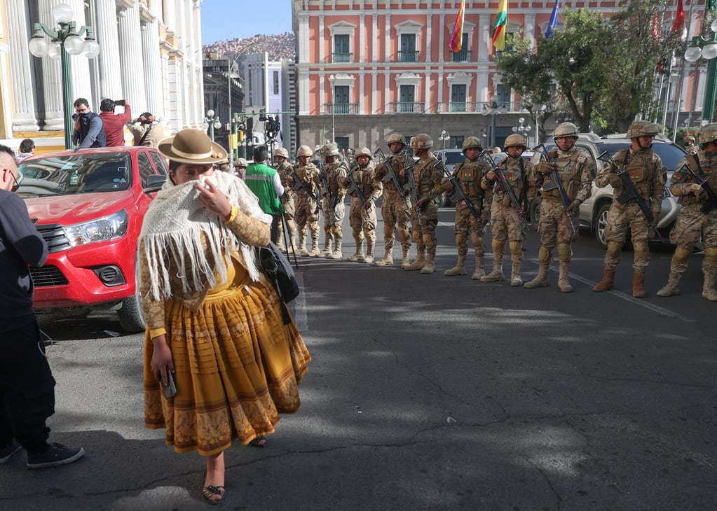 Una mujer pasa entre los militares formados frente a la sede del Gobierno de Bolivia, este miércoles en La Paz (Bolivia). El presidente Luis Arce dijo que el país "está atravesando un intento de golpe de Estado". EFE - Luis Gandarillas